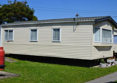 Static caravan with grass and gas cylinder outside.