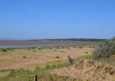 Sandy beach with distant hills under blue sky.